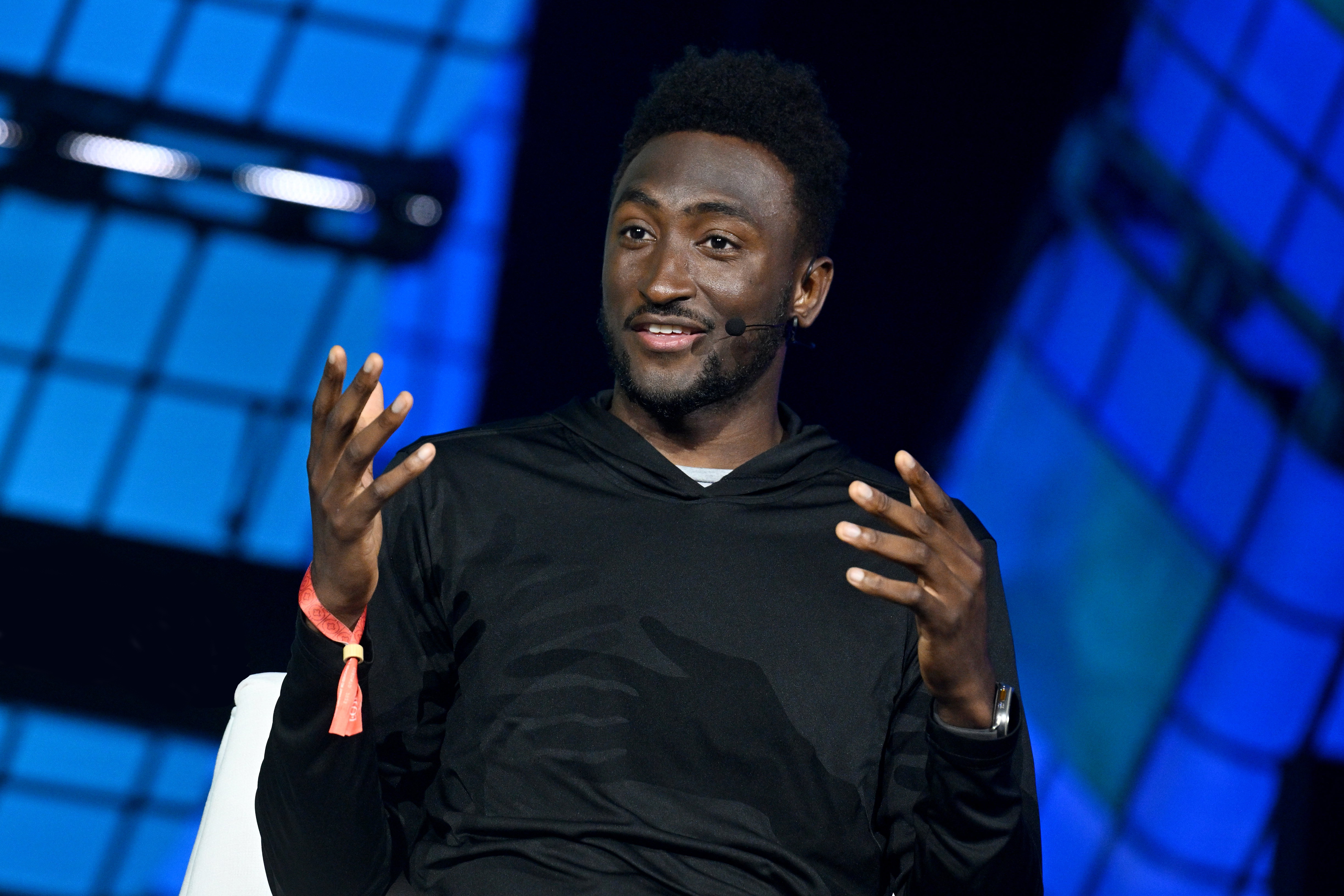 A photograph of a person, Marques Brownlee, speaking on stage at an event. They are gesturing with their hands. They appear to be sitting.